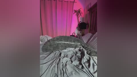 A dimly lit bedroom photo shows a disheveled bed with a large, fluffy green cushion on top, against beige curtains with pink lighting.