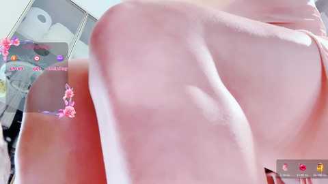 Video of a close-up, side view of a person with fair skin, wearing a pink top, and adorned with pink flower tattoos. Background shows a cluttered room with a white bed and a window.