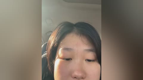 Video of a young Asian woman with long black hair, slightly tilted head, and neutral expression, sitting indoors with a blurred background.