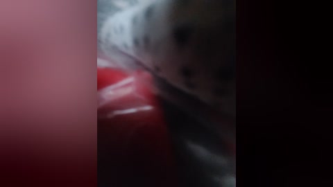 A blurry, close-up video of a person's face, partially obscured by a red object, with indistinct features and dark background.