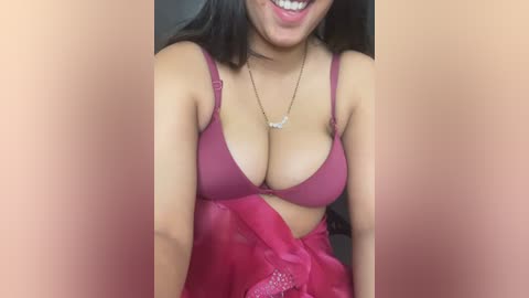Video of a smiling woman with medium skin tone, wearing a deep red bra and sheer red skirt, necklace, and earrings.