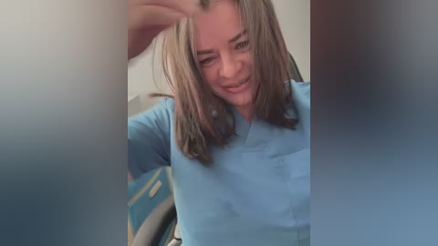 A video captures a smiling woman with shoulder-length brown hair, wearing a light blue shirt. The image is slightly blurred, with out-of-focus objects in the foreground.