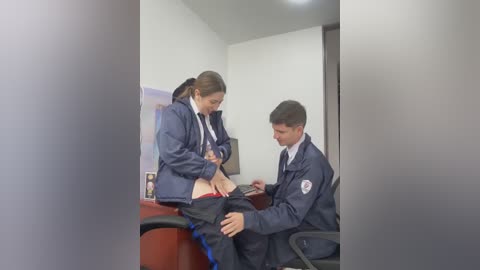 Video of two teenage girls in school uniforms, one seated on a desk, being examined by a male officer in a police uniform.