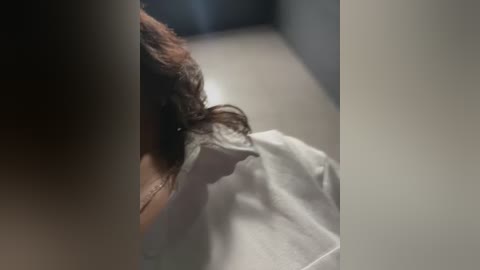 Video of a person's head with dark hair, covered in a white cloth, lying on a light-colored surface, possibly a bed or table, with blurred background.