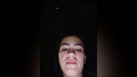 Media: A video of a young woman with medium brown skin and dark hair, looking directly at the camera. The background is dark, with a faint star visible above her head.