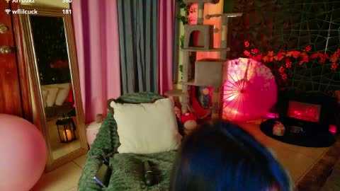 Video of a cozy, dimly lit living room with pink walls, green couch, blue curtains, and a large pink lampshade.