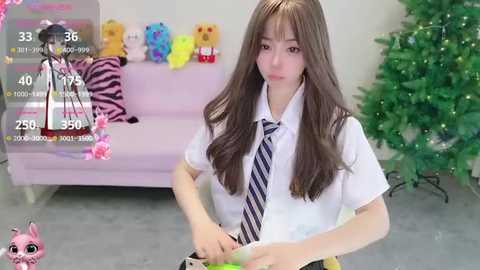 A video of a young, slender Asian woman with long brown hair and fair skin, wearing a white blouse and striped tie, stands in a brightly lit room. Behind her, a pink sofa adorned with stuffed animals, a Christmas tree, and a green plant.