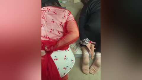 Video of two women, one in a red sari with cherry print, sitting on a bench, the other in black, with visible feet and socks.