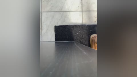Video of a sleek, modern bathroom featuring a dark marble backsplash against a light gray tiled wall. The countertop is smooth and reflective, with a wooden chair partially visible in the right corner.