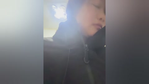 Media: A video of a young, fair-skinned person with light brown hair, wearing a black jacket, partially obscured by lens flare. Background is blurry, possibly an indoor setting.