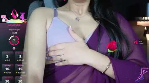 A video shows a woman with long black hair, wearing a purple shawl, exposing her left breast in a lavender bra. Background includes a dimly-lit room with a digital display and a red rose.
