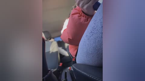 Media: A video of a plane's interior, featuring passengers' legs and seats, with a person wearing a red sweater and a blue-patterned jacket. The seats are dark blue, and the background is a blurry cabin.
