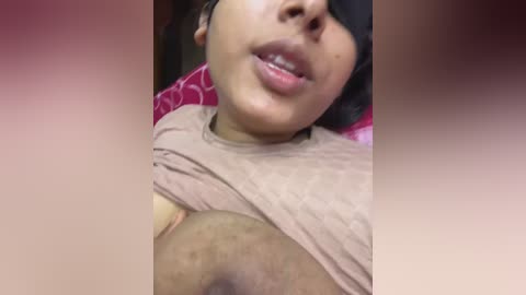 Video of a partially obscured person with medium-brown skin and dark hair, wearing a black blindfold. They have a slightly open mouth and are lifting a beige shirt, revealing a large, dark areola and nipple.