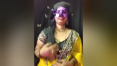 Video of a South Asian woman with dark skin, wearing a yellow sari, black headscarf, and sunglasses, dancing energetically, against a black backdrop adorned with butterflies.
