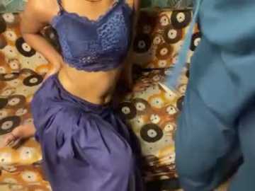 A video shows a woman in a purple lace bra and matching high-waisted skirt sitting on a patterned couch, with another person partially visible in blue clothing in the foreground.