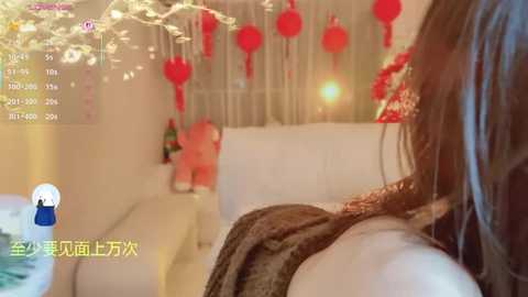 A video of a cozy, dimly lit room decorated for Christmas with white walls, red ornaments, a white couch, and a person's shoulder visible.