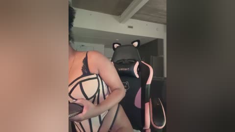 Media: Video of a woman in a black-and-white striped bra, holding a plush bear with pink accents, in a dimly-lit room with exposed wooden beams.