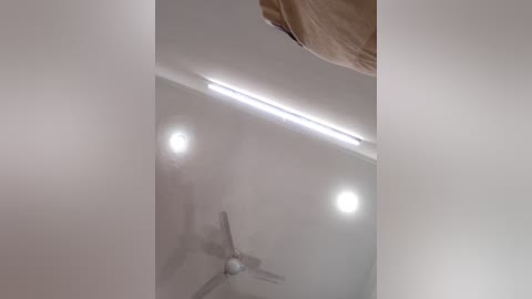 Video of a ceiling fan with three light bulbs, mounted in a white ceiling with a beige curtain partially visible on the right.