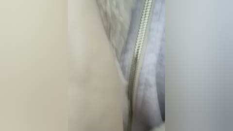 Media: Close-up video of a white, textured fabric with a visible zipper running diagonally from left to right, showcasing a subtle pattern and soft texture.