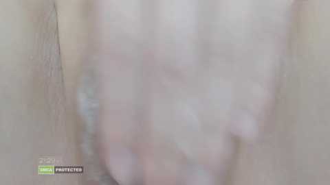 Media: A close-up video of a person's pale, hairless groin area, featuring a soft-focus, blurred texture. The image includes a watermark in the lower left corner.