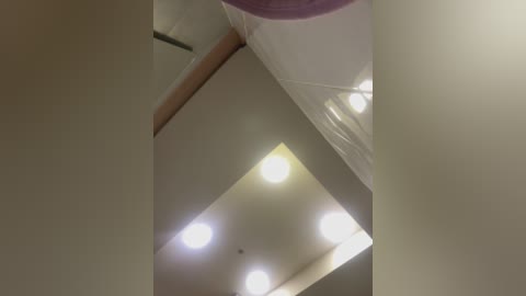 Video of a modern, minimalist ceiling with white walls and soft, diffused lighting from recessed ceiling lights. The image captures the architectural details of the ceiling and upper wall, with a slight blur due to the low angle of the camera.