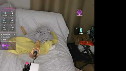 A video depicts a bed with a partially open yellow blanket, a beige pillow, and a white sheet. A virtual reality headset is plugged into a device on the bedside table, which also holds a teal glass. The room is dimly lit with beige curtains.