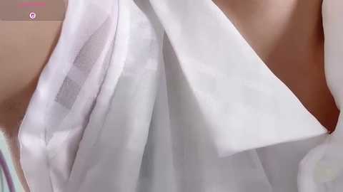 Video of a close-up of a person's arm and torso in a white robe, revealing a hint of skin, with a blurred background. The fabric is smooth and soft.