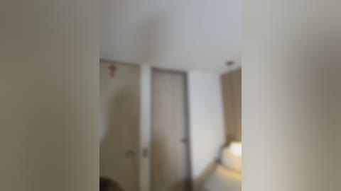 Blurry video of a modern, minimalist room with off-white walls, a door, and a lamp in the background, featuring a beige carpet and a sofa.
