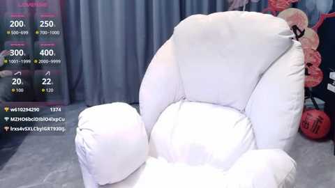 Media: Video of a plush, white, oversized armchair with soft, fluffy fabric, placed in a room with a gray curtain backdrop and red balloons. The chair is surrounded by social media-like digital overlays showing various stats and follower counts.