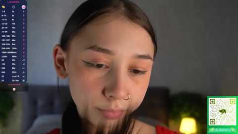 Media: Video of a young Asian woman with straight black hair, wearing a nose ring, and a green top, indoors, with a blurred background.