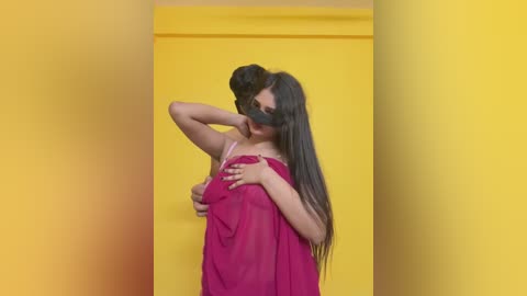 Video of a woman with long, dark hair, wearing a red sleeveless dress, with a black blindfold covering her eyes, standing against a bright yellow backdrop.