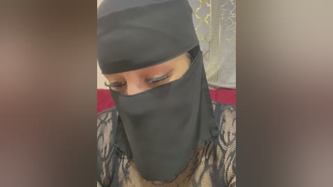 Media: A video of a woman wearing a black niqab with intricate lace sleeves, her eyes covered by a veil, set against a blurred background.