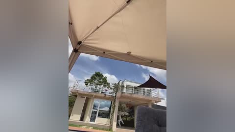 A video showing a beige patio umbrella framing a modern house with a glass balcony and a clear blue sky.