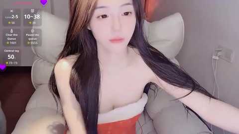 Media: A video of an Asian woman with long black hair and fair skin, wearing a red Santa hat, sitting on a white chair in a cozy room.