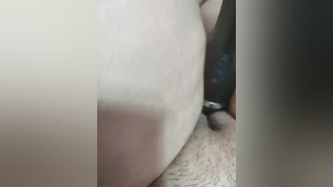 Video of a close-up of a light-skinned, hairy male torso with a penis and testicles visible, alongside a black camera lens and blurred background.