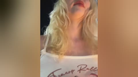 A video of a blonde woman with wavy hair, wearing a white tank top with \"Twisted Rabbits\" text, and red lipstick. The background is dark and blurred, focusing on her upper body.