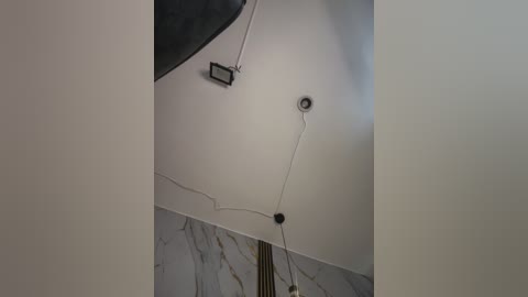 Video of a minimalist, modern room with white walls, grey marble accents, a black ceiling light, and a single white cord hanging from the center, creating a clean and sleek aesthetic.