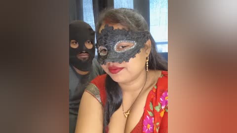 Video of a woman in a red dress with a floral pattern, wearing a black lace mask, and a man in a black mask, both indoors near a window.