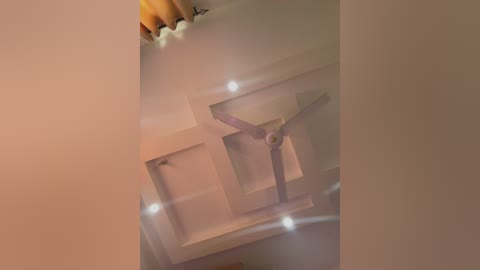 Media: Video of a beige ceiling with a white ceiling fan, surrounded by soft, warm lighting and a brown curtain partially visible in the top left corner.