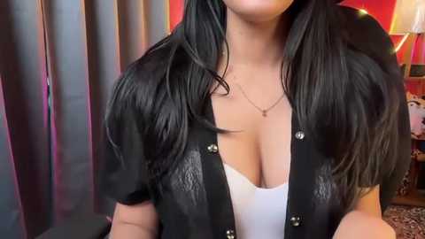 Video of a woman with long black hair, wearing a low-cut black leather jacket over a white top, against a red and black background.