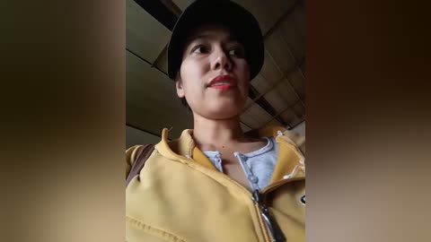 Video of a young woman with light skin, wearing a black helmet, yellow jacket, and a blue shirt, looking up with a neutral expression.