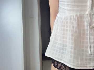 Video of a woman's torso in a sheer white blouse, revealing black lace panties underneath, against a light gray wall.