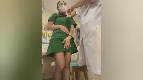 Video of a slender, light-skinned woman in a green medical uniform, with glasses, a mask, and black stockings, being touched by a male doctor in a white coat.