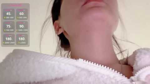 Video of a woman's neck and shoulders wrapped in a white towel, displaying a digital health app with heart rate and blood oxygen level data.