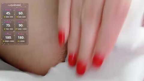 A video of a person with fair skin, lying on white sheets. Their hand, with red-painted nails, rests on their groin area, which has a small amount of pubic hair. A temperature gauge in the top left corner shows 180 degrees Fahrenheit.