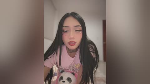 Media: Video of an Asian woman with long black hair, wearing a pink t-shirt with a panda graphic, makeup, and a tattoo on her neck, indoors with blurred background.