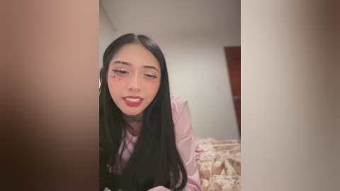 Media: A video of an Asian woman with long black hair, wearing pink lipstick, lying on a bed with a beige blanket. The image is cropped and partially blurred, focusing on her face.
