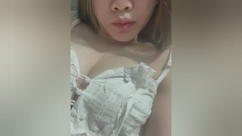 Video of a light-skinned woman with straight, shoulder-length blonde hair, wearing a white lace bra with a torn strap. Her lips are slightly parted, and her face is partially obscured by the frame.