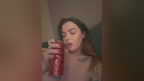A video of a woman with fair skin and long brown hair, wearing a floral top, drinking from a red can, with a tattoo on her left shoulder.