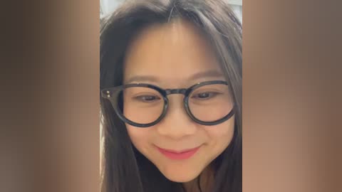 Video of a young Asian woman with long black hair, wearing black-rimmed glasses and a slight smile. The background is blurred, with warm tones.